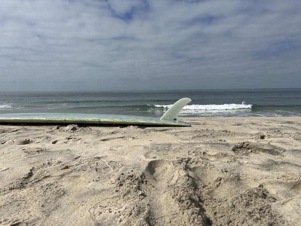 Bing Pivot fin in a green surfboard on the beach.