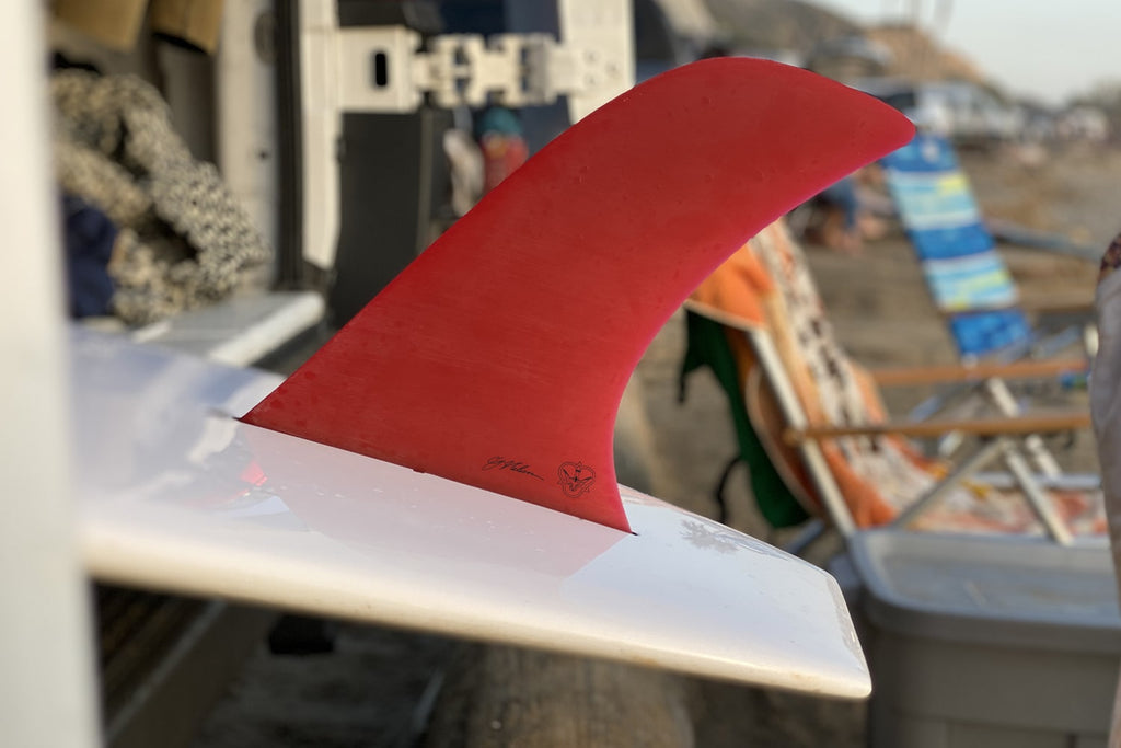 A red CJ Noserider fin, on a white surfboard, in the back of CJ's van.