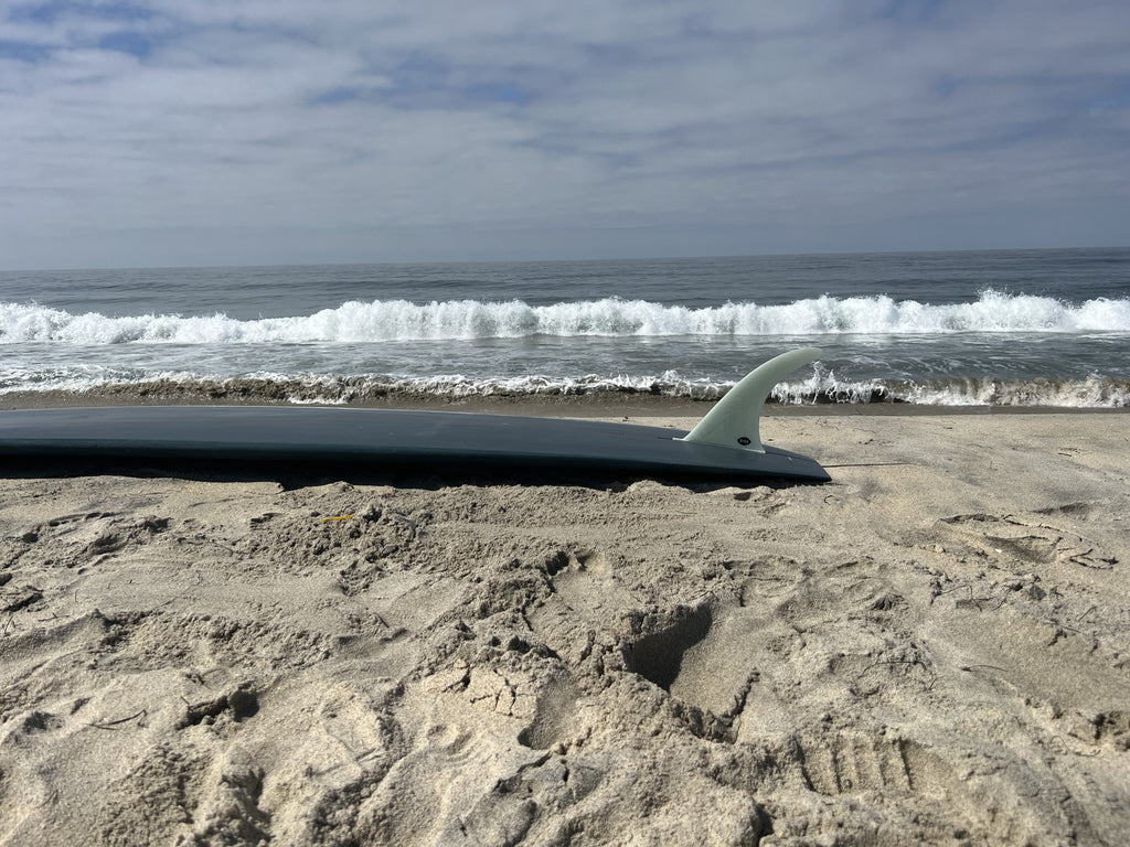 Bing Flex fin in a dark gray surfboard on the beach.