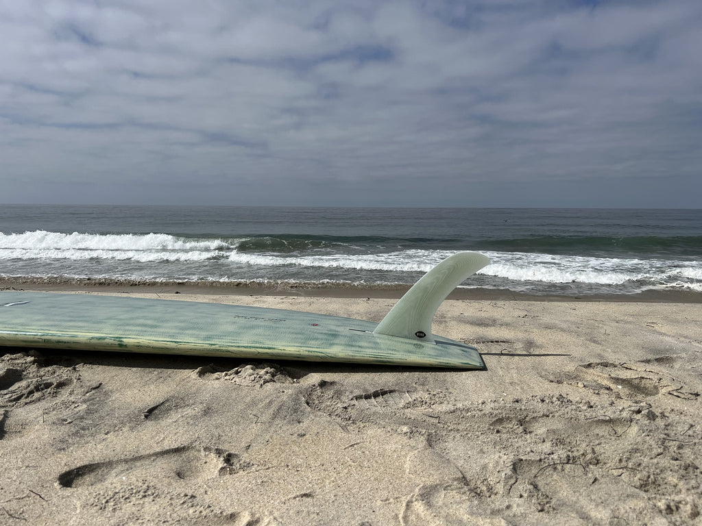 Bing Trim Pivot fin in a green surfboard on the beach.