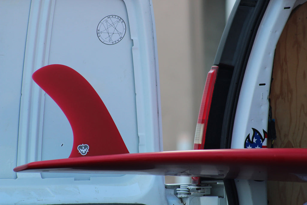 A red CJ Cali Pivot on a red longboard popping out the back of a van.