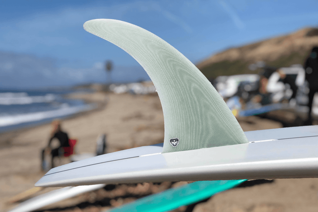 CJ clear volan Involvement fin on a white surfboard on the beach.