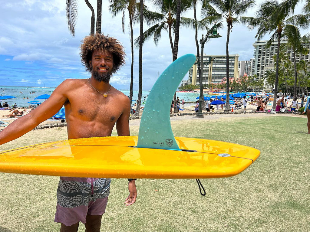 Kani Stewart in Hawaii holding his yellow board with his Waikiki blue fin.