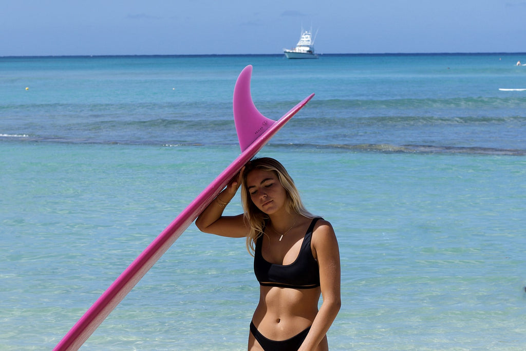 Keani catches some shade under her board on the beach in Hawaii with her new pink fin model.
